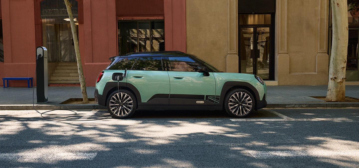 Side view of the all-electric MINI Aceman in Ocean Wave Green with Black Roof charging on the street.
