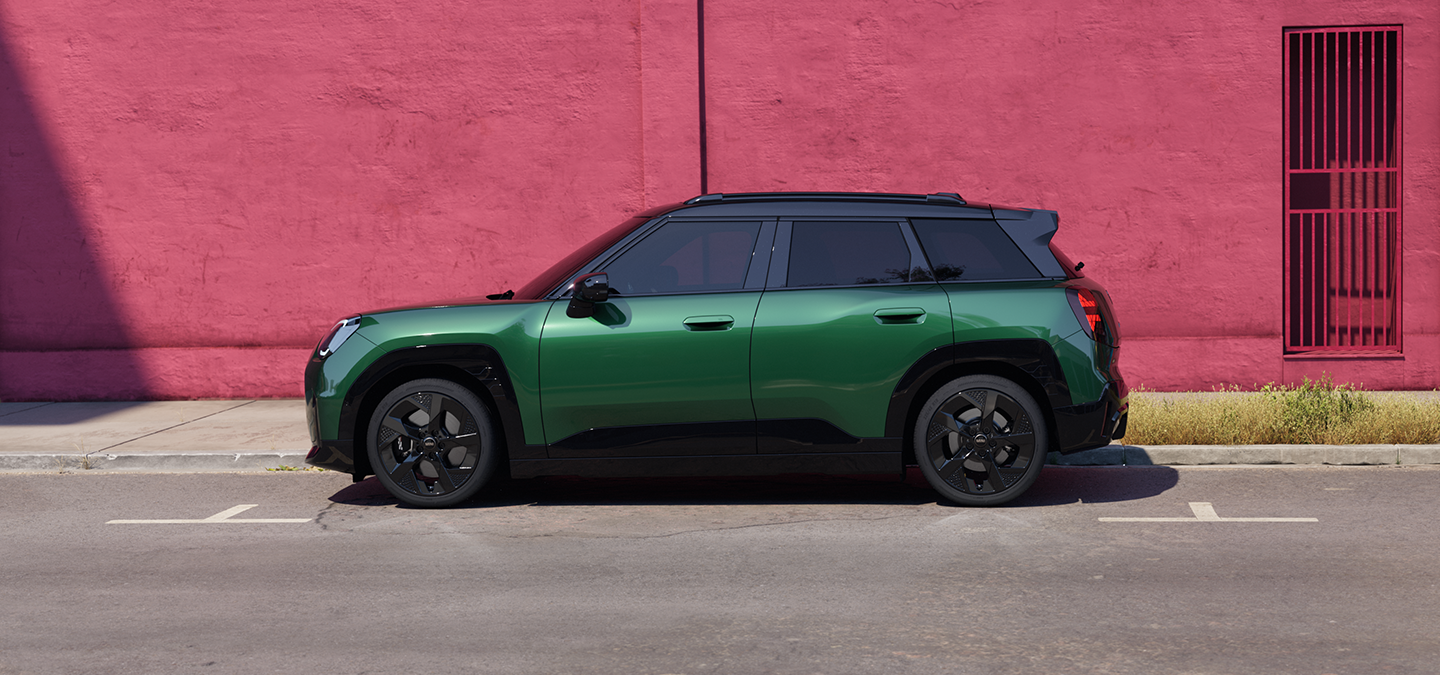 Side view of the all-electric MINI Aceman in British Racing Green and Black Roof, on a street.