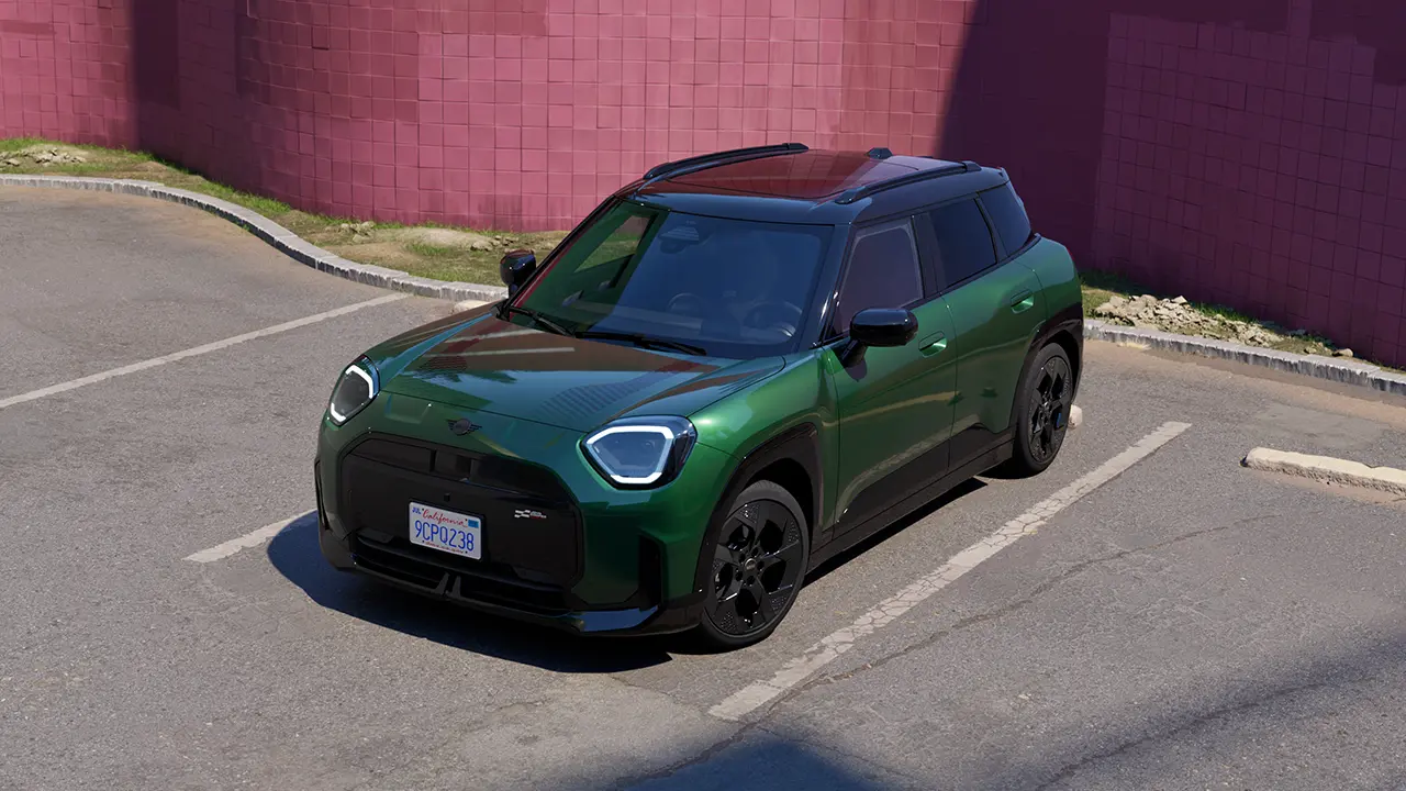 Front view of parking all-electric MINI Aceman in British Racing Green in car park with pink wall in the background