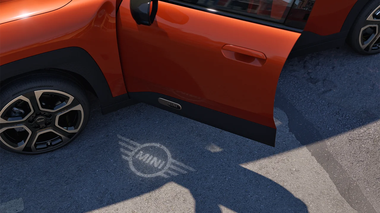 Exterior view of all-electric MINI Aceman with open door and MINI logo welcome light on the ground