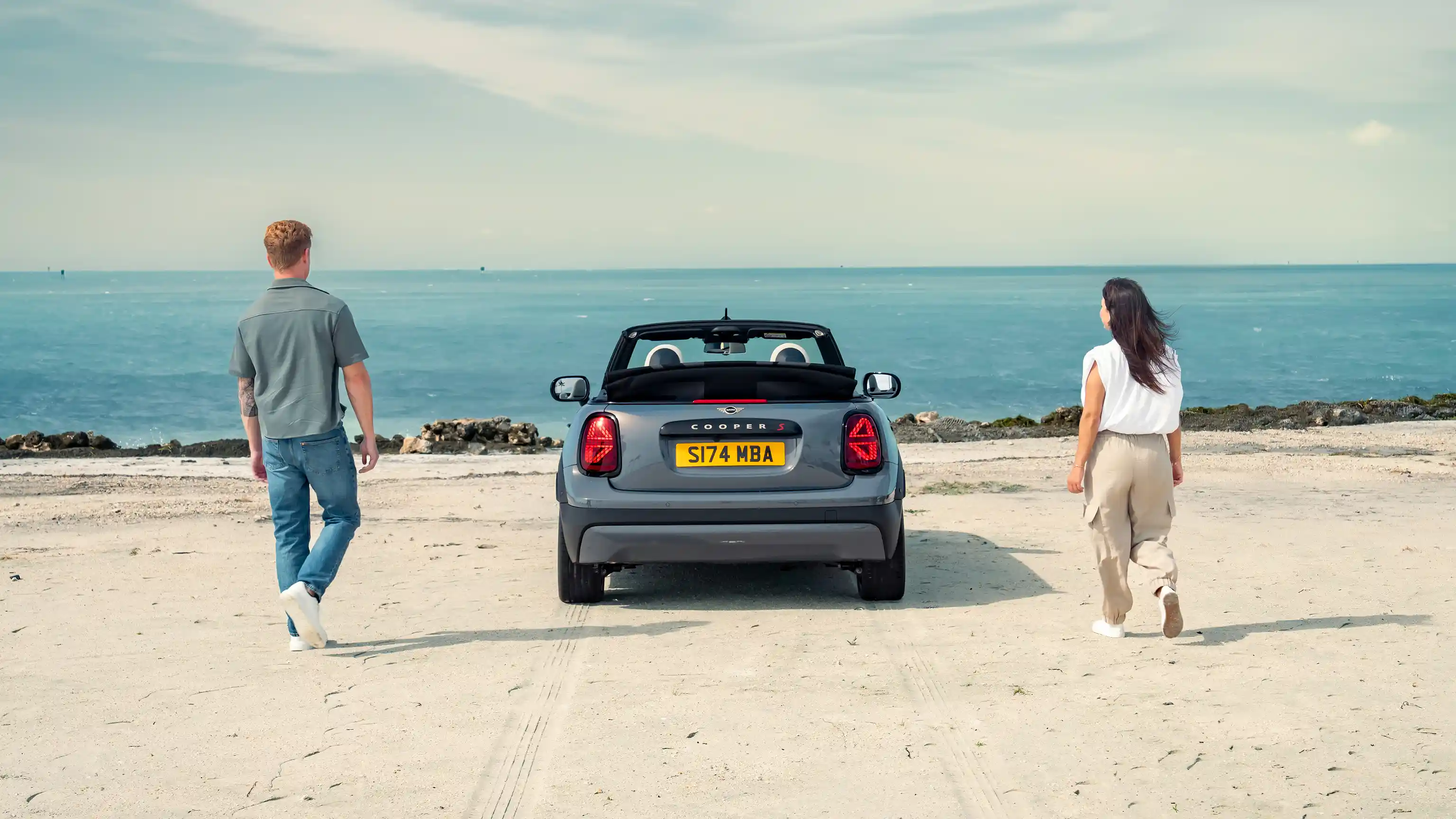 Rear view of a parked MINI Cooper Convertible on a beach with two people