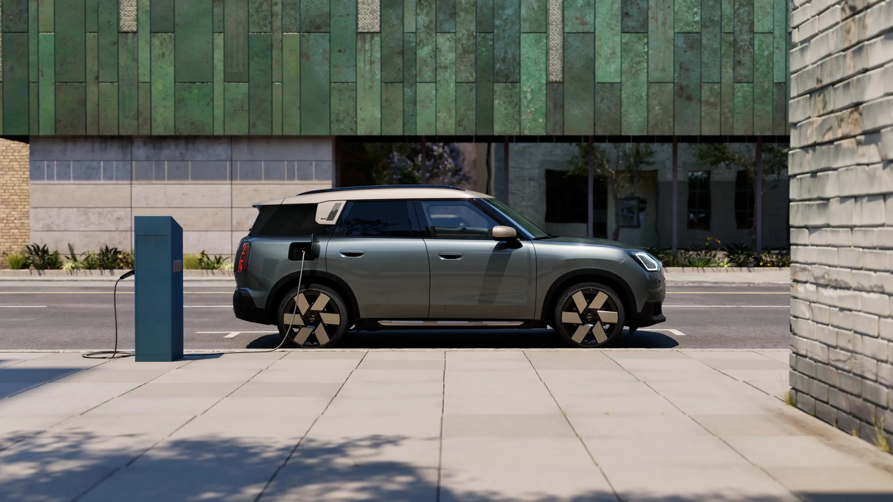 Side view of a charging all-electric MINI Countryman in Smokey Green with Vibrant Silver Roof on the street