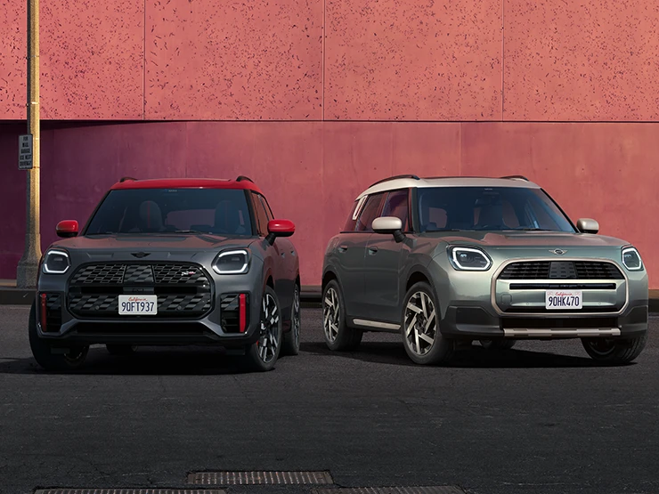 Front view of the MINI Countryman JCW in Legend Grey and Red Roof and the MINI Countryman in Smokey Green and Vibrant Silver Roof standing next to each other.