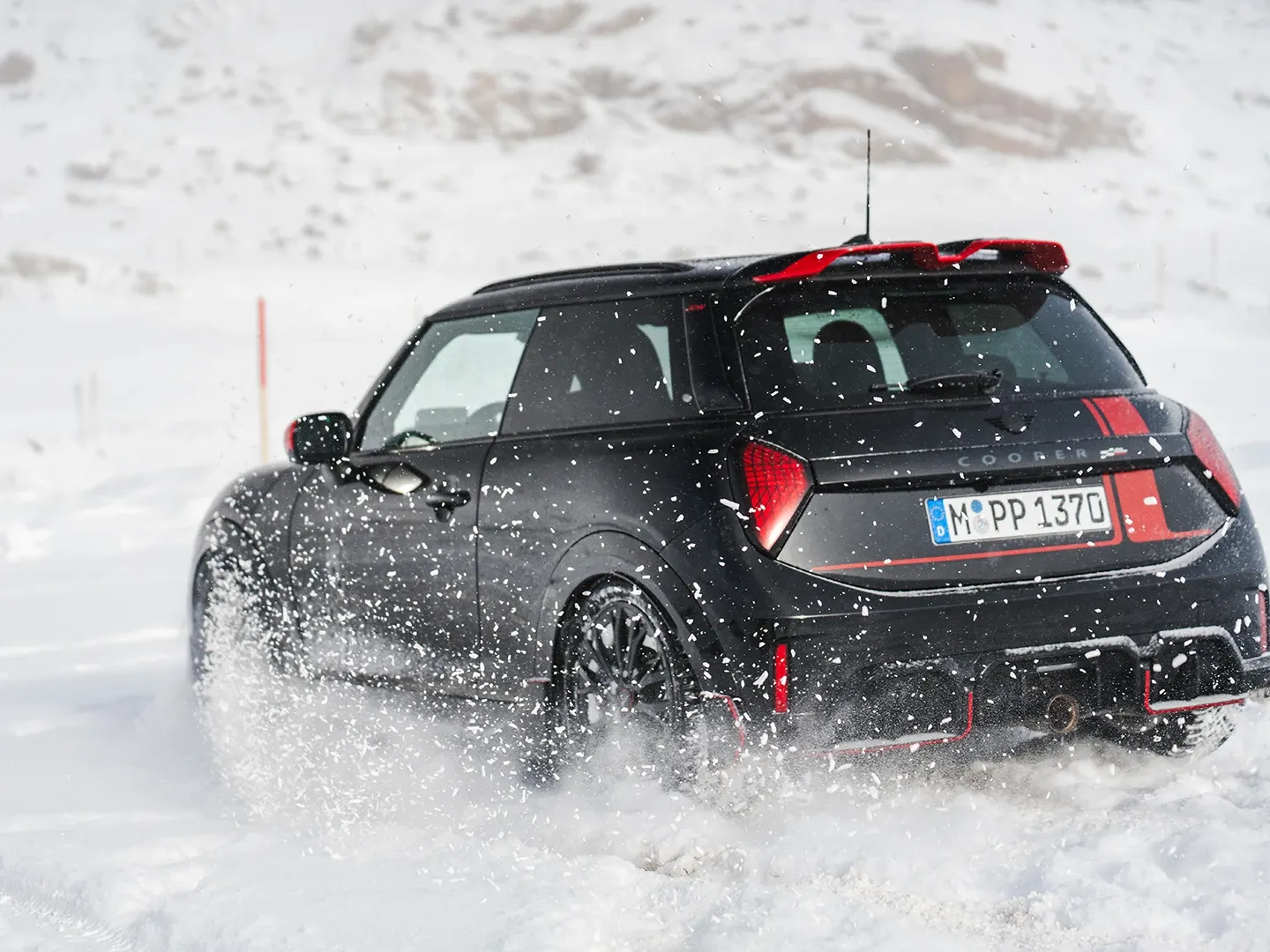 Rear view of a MINI Cooper JCW driving through the snow.
