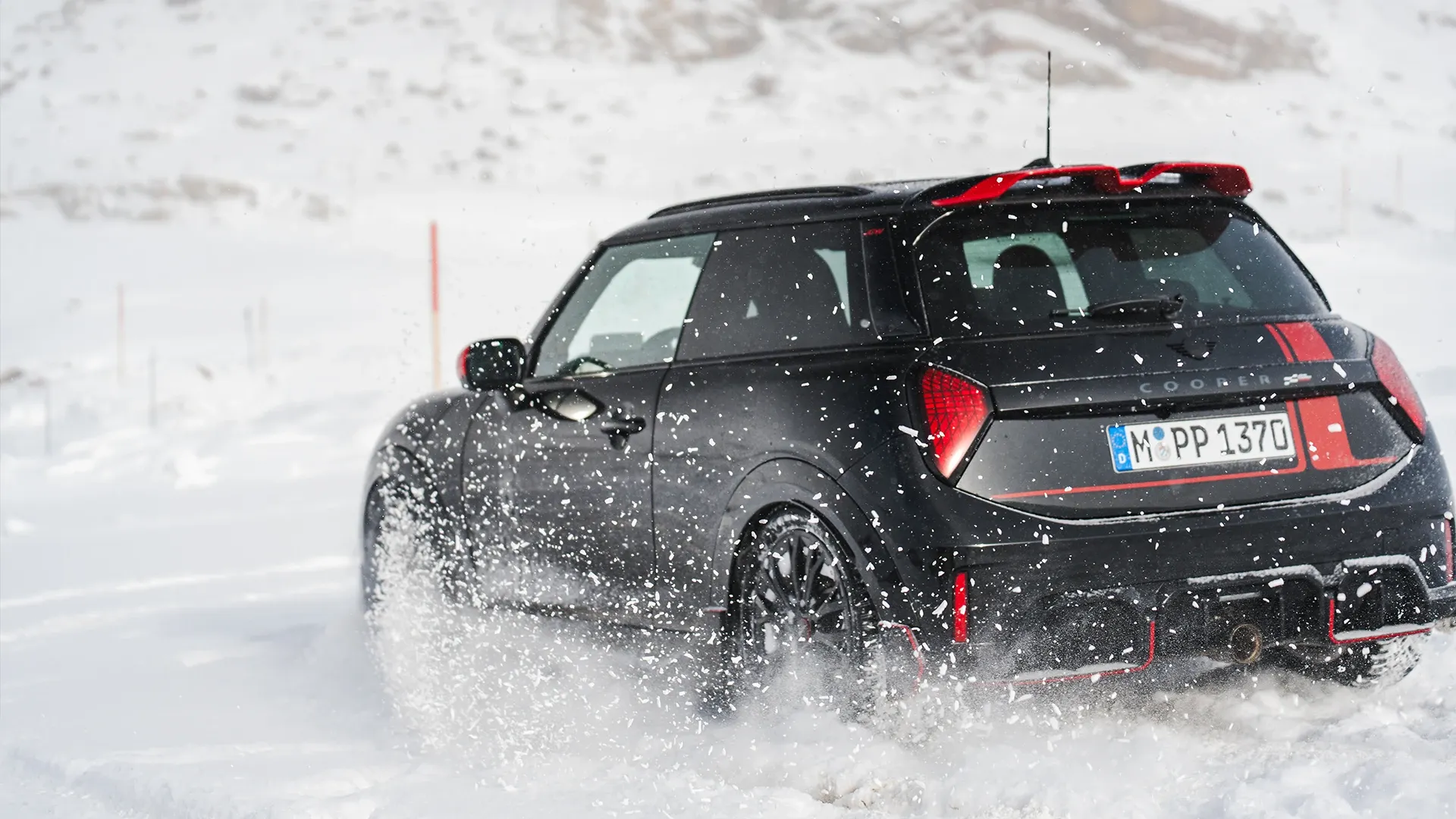 Rear view of a MINI Cooper JCW driving through the snow.