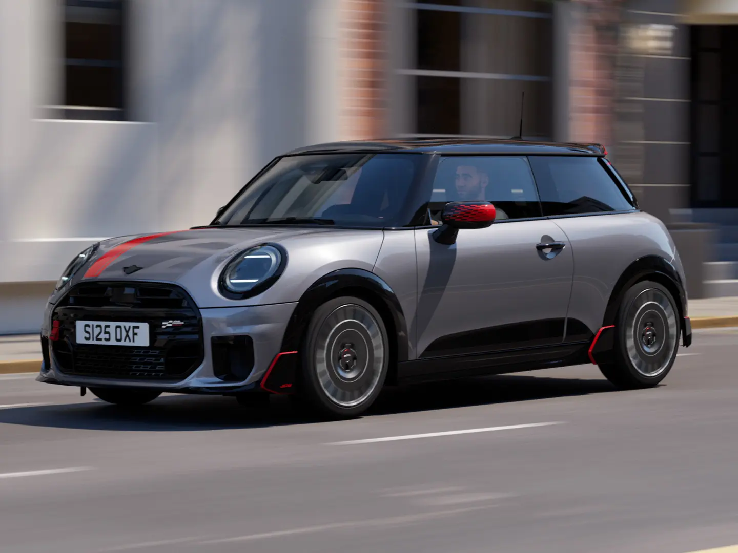 MINI Cooper 3-door in Melting Silver with John Cooper Works mirror cap and bonnet decal in Chili Red, roof spoiler and winglet in Black, driving along a city street – front-side view.