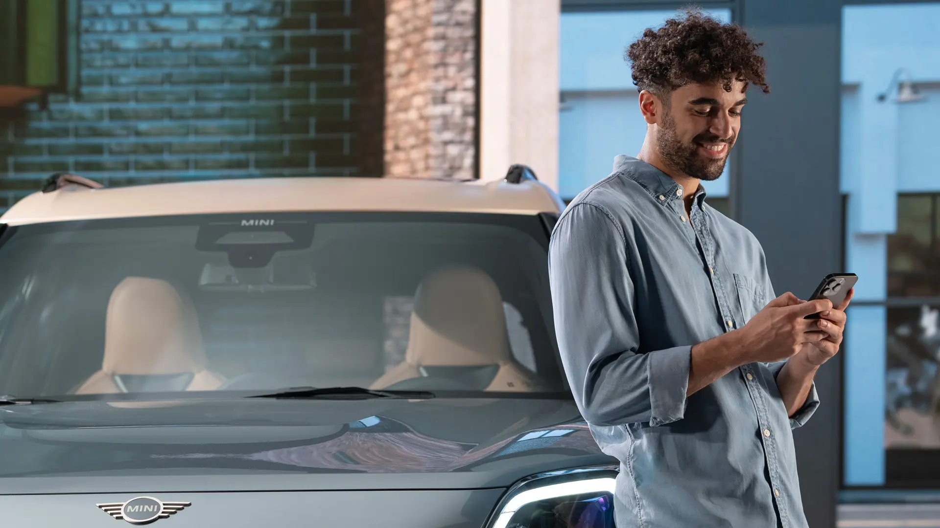 MINI personalised service appointments - a man typing on his phone next to a MINI