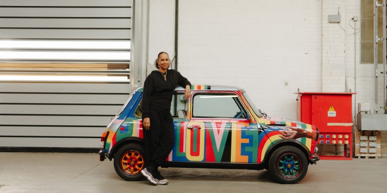 Lawena stands in front of her designed and colourful Mini classic. The side of the car reads “BIG LOVE”. 