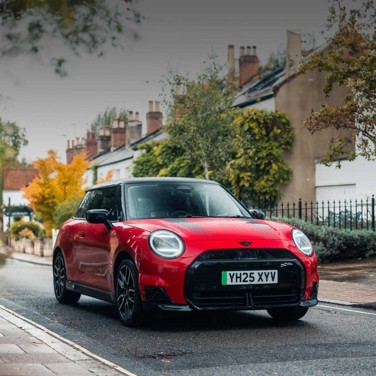 A yellow MINI Cooper car parked on a cobblestone street beside brick buildings.
