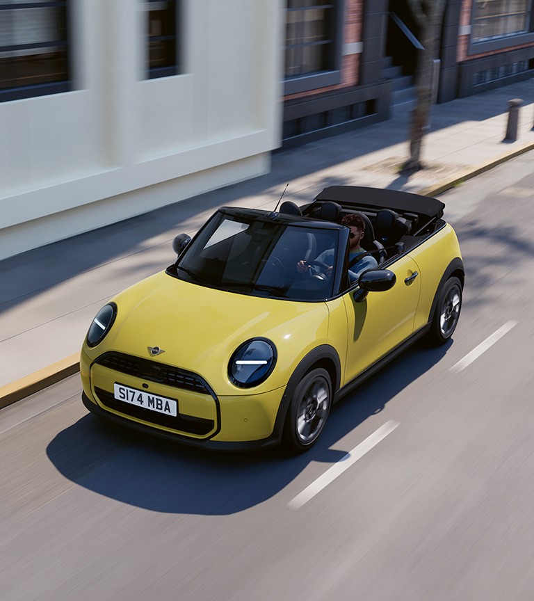 The new MINI convertible in yellow is cruising along a road, highlighting its stylish features and open-top design.