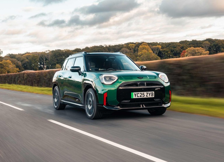 Front view of parking all-electric MINI Aceman in British Racing Green in car park with pink wall in the background